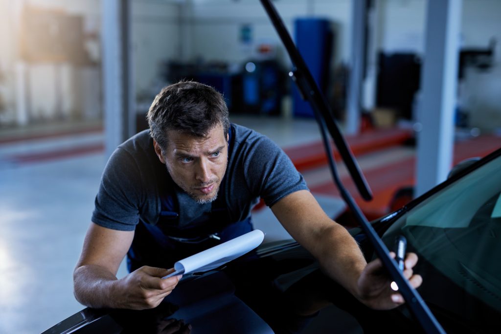 auto repairman examining a car while working at workshop.